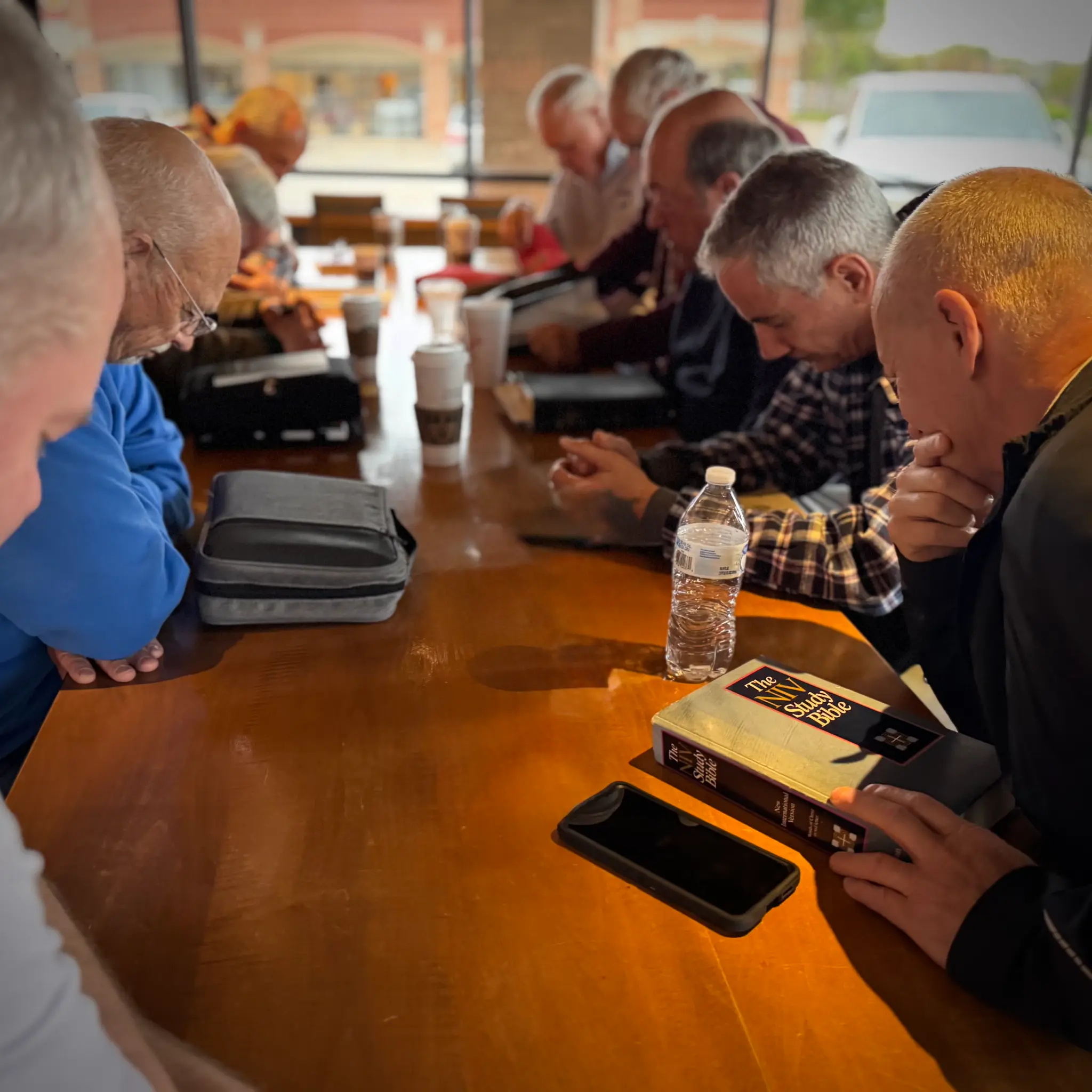 Men gathered around a table in prayer during Bible study